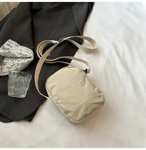 Detail view of a beige waterproof nylon crossbody bag with adjustable wide strap on a table