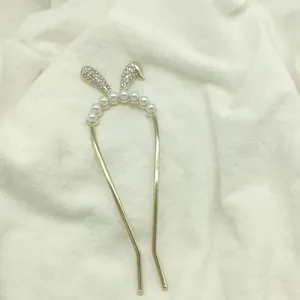 Close-up of golden U-shaped hair pin with rhinestone bunny ears and white faux pearls