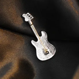Vintage silver electric guitar brooch with secure golden pin clasp on silk background