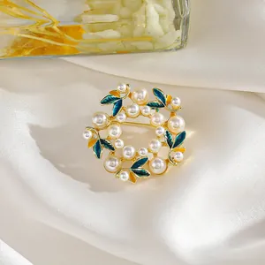 Elegante broche de corona floral con perlas y esmalte verde esmeralda sobre seda blanca