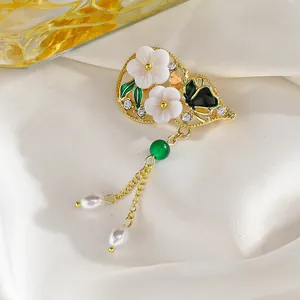 Detalle de broche floral con conchas blancas, mariposa negra y perlas verdes de lujo