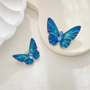 Elegant butterfly brooches featuring green enamel wings and blue crystal accents on white decor