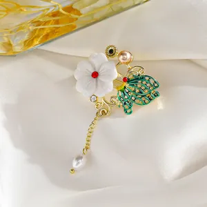 Detalle del broche de flor y mariposa con esmalte verde, perlas y borlas de cadena dorada