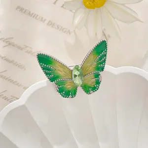 Macro detail of green enamel butterfly brooch with marquise-cut gemstone on white shell