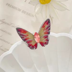 Macro detail of a small butterfly brooch featuring red-yellow enamel and a pink crystal