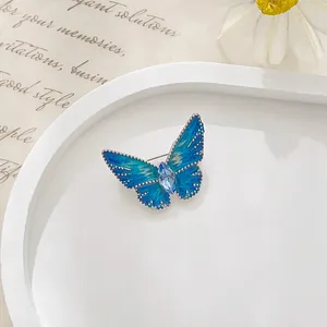 Detail view of a refined butterfly brooch with blue enamel wings and a center gemstone