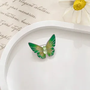 Close-up of green butterfly brooch with enamel finish and a green gemstone on white tray