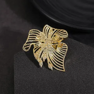 Elegant gold hollow leaf brooch with emerald marquise stones on textured gray surface