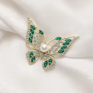 Elegant gold butterfly brooch with green rhinestones and a white pearl on white silk