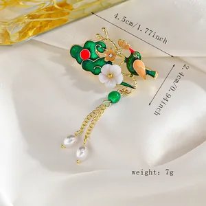 Detalle de broche de esmalte con pájaro verde y flor blanca con borlas de perlas
