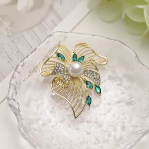 Macro detail of golden flower brooch with emerald marquise stones and center pearl