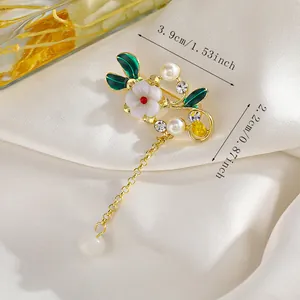 Primer plano de broche floral verde con perlas y cadena dorada sobre seda blanca