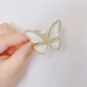 Elegant gold butterfly brooch with white enamel, crystal edges, and large center pearl