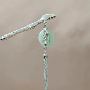 Close-up of silver bamboo style hair pin with green jade stone and long metal tassels