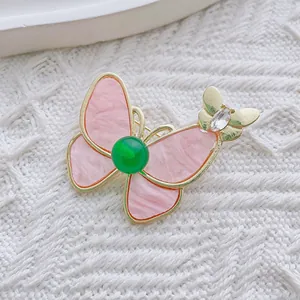Makrodetail einer hochwertigen Schmetterlingsbrosche mit rosa Marmorflügeln und grünem Stein