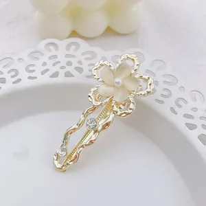 Detalle de horquilla de flor dorada con pétalos de piedra ojo de gato y perla en bandeja blanca