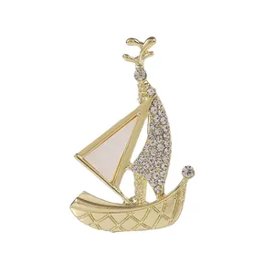 Golden sailboat brooch with sparkling rhinestones and white enamel finish on white background