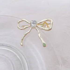 Detalle de pinza para el pelo con lazo de metal líquido dorado y piedra de corazón