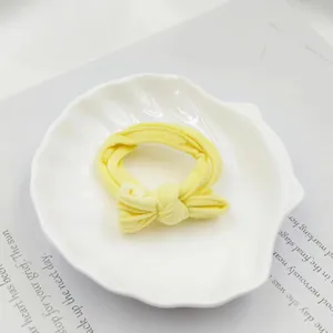 Close-up of a bright yellow fabric bow scrunchie on a decorative white shell tray