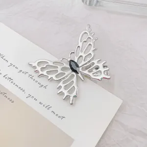 Detalle de pinza para el pelo de mariposa plateada con alas caladas y piedra negra central