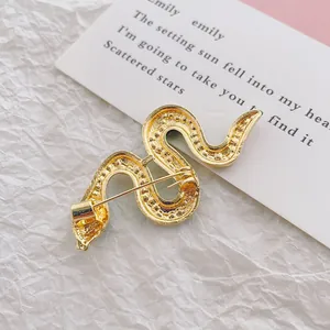 Back view of a gold snake brooch with textured finish and safety pin clasp on white paper