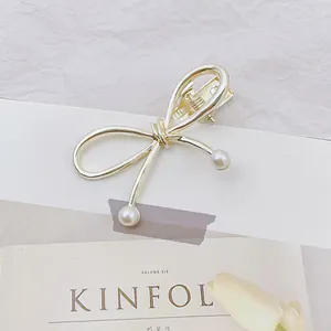 Detalle de una pinza para el cabello de metal dorado con perlas blancas y clip de pato