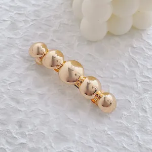 Vue détaillée de la barrette à billes dorées polies sur un fond blanc texturé élégant