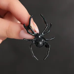 Broche araignée noire Halloween avec paillettes vertes tenue à la main pour la taille