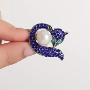 Exquisite fox brooch with blue crystals and a pearl accent, shown in hand for size