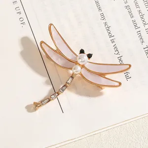 Exquise broche libellule dorée avec ailes roses et perles sur une page de livre ancien