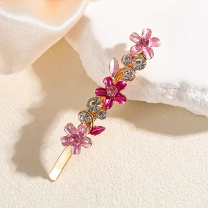 Dettaglio di un fermaglio per capelli dorato con tre fiori in smalto rosa e strass brillanti