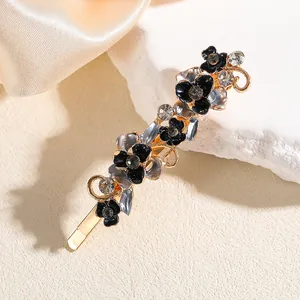Dettaglio macro della molletta a fiori dorati con petali in smalto nero e cristalli