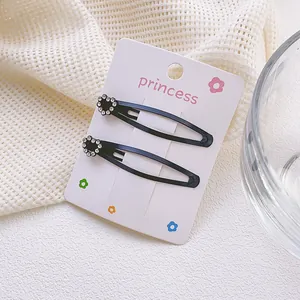 Detalle de dos pinzas para el cabello negras con flores de diamantes en cartón rosa