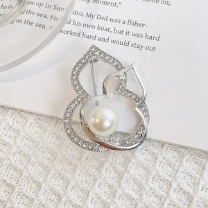 Broche gourde argentée avec cristaux et perle blanche sur un fond de livre élégant