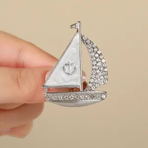 Spilla a barca a vela argentata con smalto bianco e strass tenuta in mano