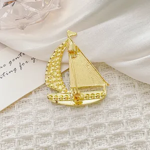 Elegante spilla a forma di barca a vela dorata con strass su tessuto bianco strutturato
