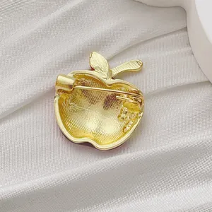 Back view of golden apple brooch with pin clasp on white silk background