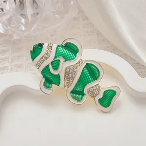 Primer plano de broche de pez en esmalte verde con pedrería sobre fondo blanco