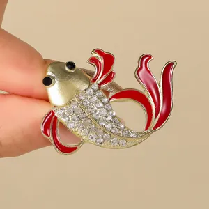 Primer plano de un broche de pez dorado con esmalte rojo y cristales brillantes