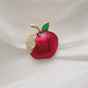 Detail of red enamel apple brooch with sparkling white rhinestones on silk fabric
