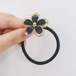Détail d'un élastique à cheveux noir avec fleur aux bords dorés et strass blancs