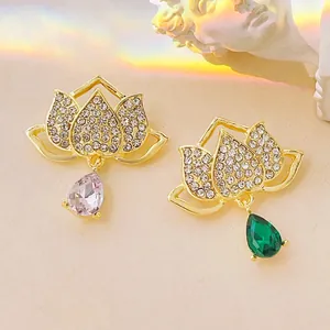 Elegant gold lotus brooch with emerald and pink crystal pendants on a textured background