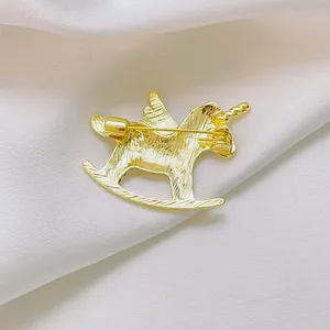 Golden unicorn rocking horse brooch with pin fastening on white silk background