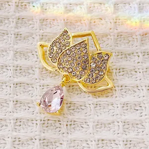 Elegant lotus flower brooch with pink teardrop crystal on white tweed background