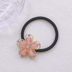 Gros plan d'un chouchou fleur en strass rose avec élastique noir sur un fond blanc