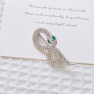 Macro shot of silver snake brooch with white rhinestones and green emerald eyes