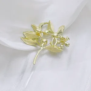 Elegant gold leaf brooch with brushed metal texture displayed on soft white silk fabric