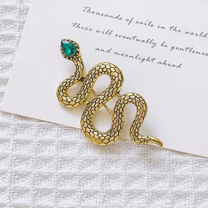 Detailed macro of vintage gold snake brooch with green gemstone on textured white background