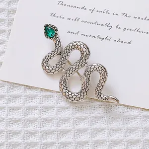 Detail of silver snake brooch featuring a green teardrop gemstone and scale texture