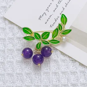 Elegant gold blueberry brooch with green leaves and purple beads on white texture